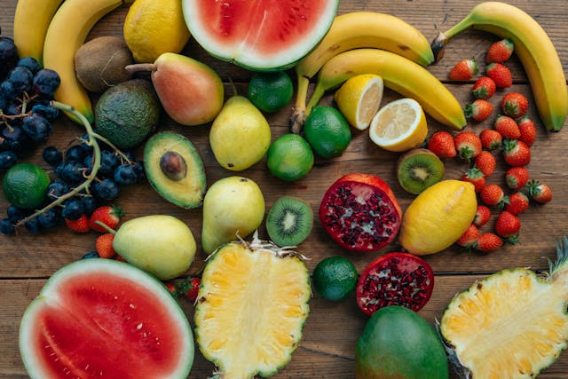 Colorful assortment of fresh fruits on wooden counter: grapes, watermelon, pear, banana, strawberry, pomegranate, pineapple, lime. Natural vitamin source for energy.