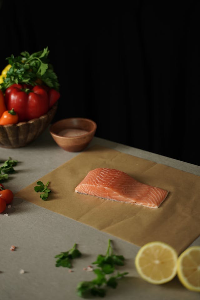 A plate with a piece of red fish, sliced lemon, fresh vegetables, and greens, representing a high-quality source of protein and Omega-3 fatty acids for the Metabolic Reset Diet.