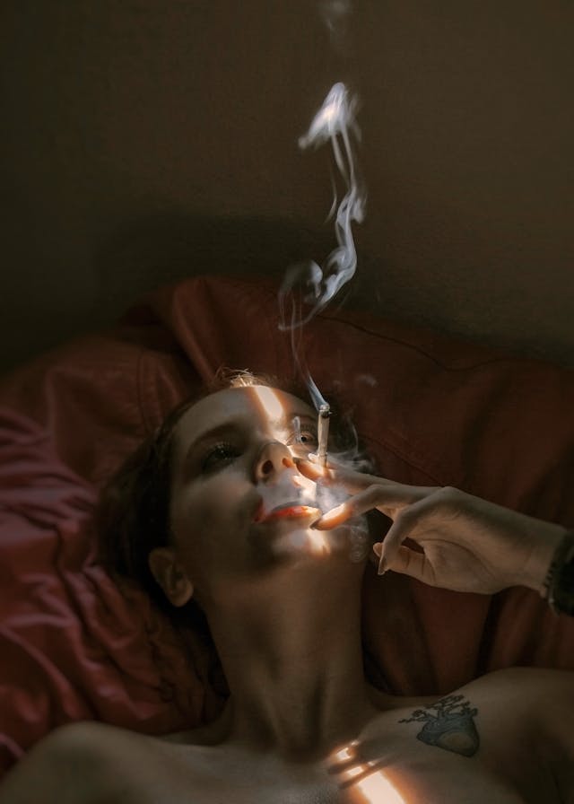 A person smoking a cigarette in bed, symbolizing chronic stress. This illustrates how stress elevates cortisol, leading to increased belly fat accumulation.