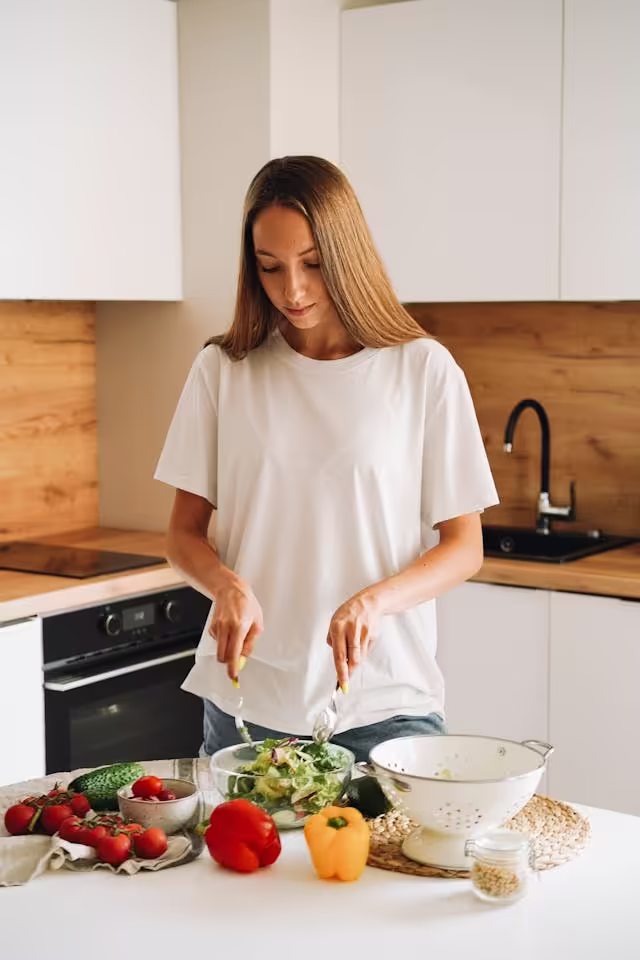 Young woman preparing fresh vegetable salad for healthy dinner with tomatoes, cucumbers, bell peppers, and greens