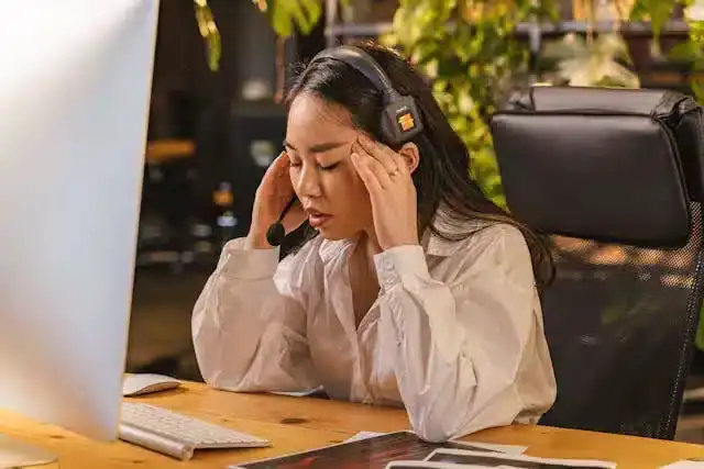 Office worker woman holding her head in pain due to neck and headache fatigue from prolonged sitting, posture correction resistance band