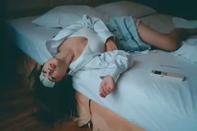 Woman lying on bed with a thermometer and air conditioner remote, illustrating Sleep Hygiene for Menopause and the impact of sleep disorders, hormonal changes, and body temperature regulation