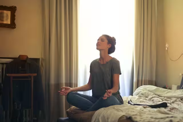Woman sitting comfortably on bed practicing breathing exercises to manage anxiety, related to CBT for Anxiety Worksheets
